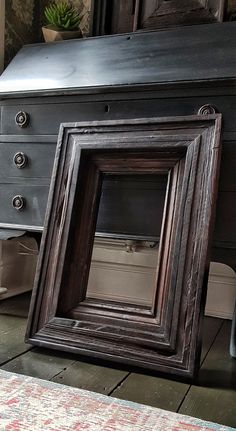 an old photo frame sitting on the floor in front of a dresser with drawers and a potted plant