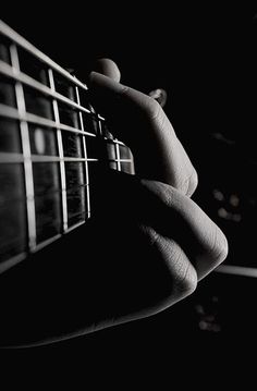 a black and white photo of someone's hand holding an acoustic guitar in the dark