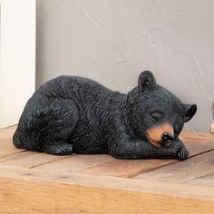 a black bear statue laying on top of a wooden table next to a potted plant