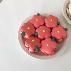 there are some pink and green decorated cookies on a plate next to a bowl of cupcakes