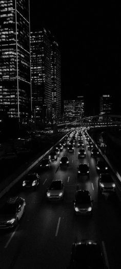 black and white photograph of cars driving down the highway at night time with skyscrapers in the background