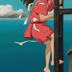 a girl in a red dress is standing on a railing and looking out at the ocean