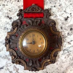 an antique clock with a red ribbon around it on a marble counter top, showing the time in roman numerals