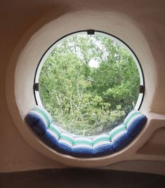 a round window with blue and green cushions on the outside, looking out onto trees