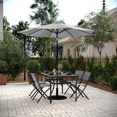 a patio table with chairs and an umbrella in the middle on a brick patio surrounded by greenery