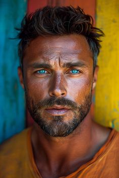 a man with blue eyes and beard standing in front of a colorful wall looking at the camera