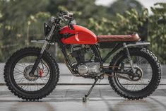 a red and black motorcycle parked on top of a cement ground next to trees in the background