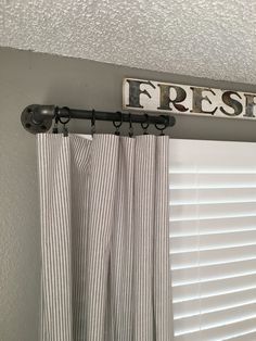 a sign that says fresh hanging on the wall above a window with curtains in front of it