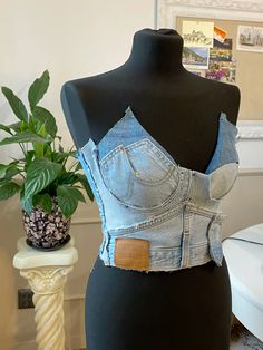 a black mannequin with a blue jean top on it's torso and a potted plant in the background