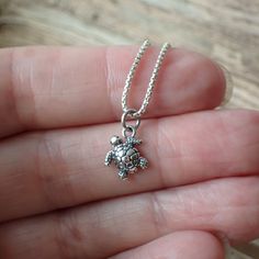 a person holding a tiny turtle necklace in their hand