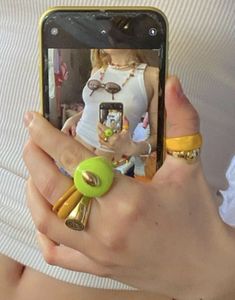 a woman taking a photo with her cell phone while wearing rings and bracelets on her wrist