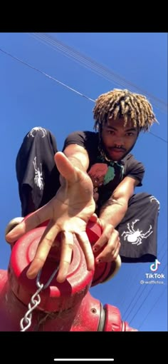 a man with dreadlocks sitting on top of a red fire hydrant