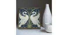 two white swans on blue and gold tile next to a vase