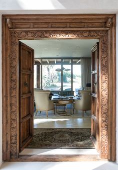 an open wooden door leading to a living room with chairs and a table in it