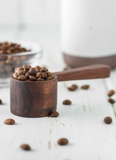 a wooden spoon filled with coffee beans on top of a white table next to a glass bowl