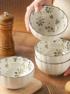 three white bowls with yellow flowers are sitting on a wooden table next to utensils