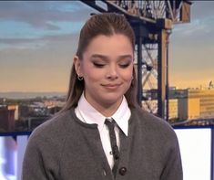 a woman with long hair wearing a gray sweater and black tie is smiling at the camera