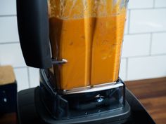 a blender filled with orange juice on top of a wooden table next to a white tiled wall