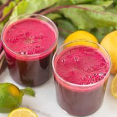 two glasses filled with beet and lemon smoothie next to some fresh fruit on the table