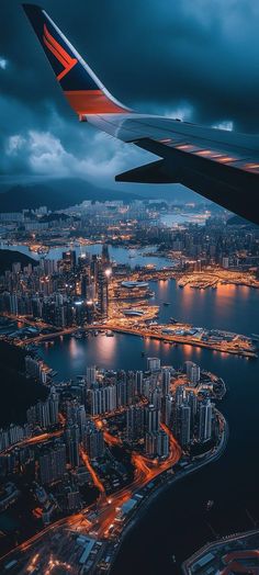 an airplane wing flying over a large city at night with lights on the water below