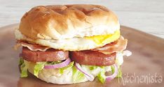 a bacon, egg and lettuce breakfast sandwich on a brown plate with white wood background