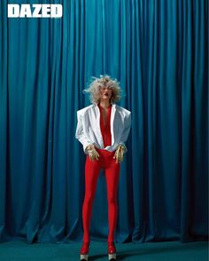 a woman in red pants and white shirt posing for a photo with blue curtains behind her