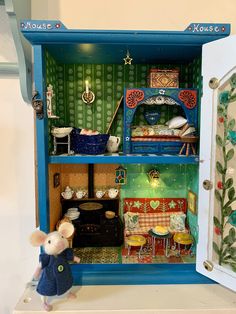 a toy mouse is standing in front of a doll house with furniture and accessories inside