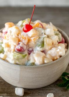 a bowl full of fruit salad with a cherry on the top and marshmallows around it