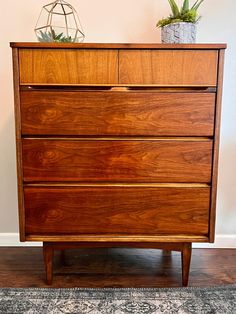 a wooden dresser sitting on top of a hard wood floor next to a white wall