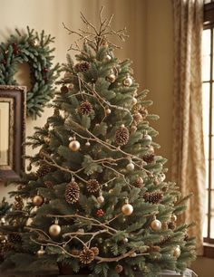 a small christmas tree with pine cones and ornaments on it in front of a window