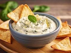 a blue bowl filled with dip surrounded by tortilla chips on a wooden platter