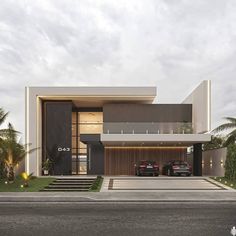 two cars are parked in front of a modern house with palm trees and grass on the side