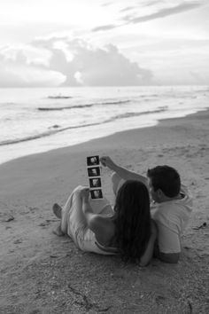 a man and woman laying on the beach holding up a sign