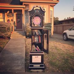 an old fashioned clock sitting on top of a book shelf in front of a house