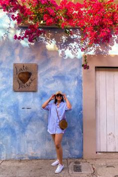 a woman standing in front of a blue wall with pink flowers hanging from the ceiling