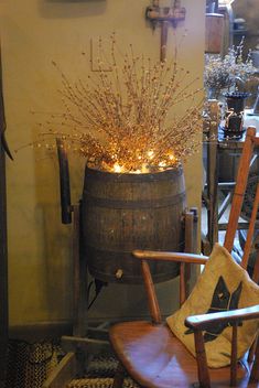 a wooden chair sitting in front of a barrel filled with branches and lights next to a window