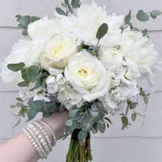 white flowers and greenery in a vase held by a woman's hand on a brick wall