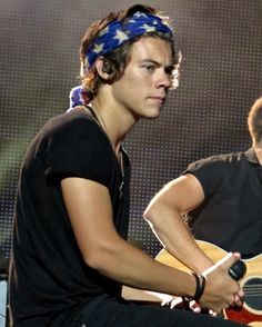 two young men playing guitars on stage with one wearing a bandana and the other holding an acoustic guitar