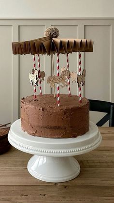 a chocolate cake on a white pedestal with three candles in the shape of an airplane