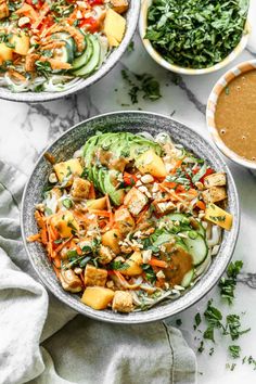 two bowls filled with vegetables and sauces on top of a marble countertop next to another bowl full of salad