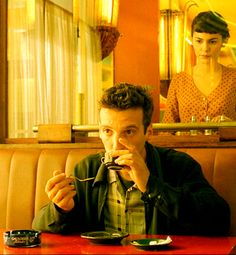 a man sitting at a table in front of a woman eating food with chopsticks