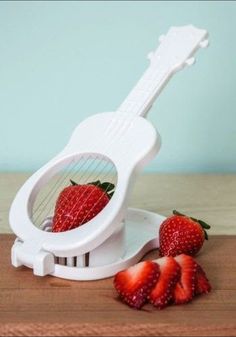 strawberries sit next to an electric ukulele on top of a wooden table