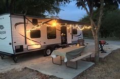 a camper trailer with lights strung from it's roof and picnic table in the foreground