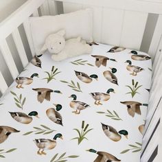 a crib bed with ducks on it and a teddy bear sitting next to the crib