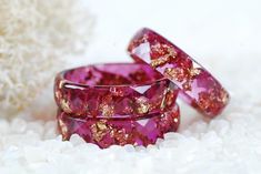 two pink rings with gold flecks on them sitting on some white rocks and sand