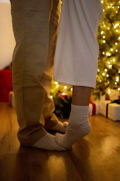 two people standing next to each other in front of a christmas tree