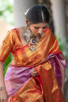 a woman in an orange and pink sari with jewelry on her neck, standing next to a tree