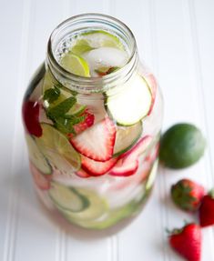 a mason jar filled with sliced strawberries, cucumbers and limes on a white table