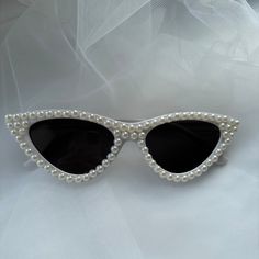 a pair of white sunglasses with pearls on the sides and black lenses, sitting on a white background