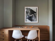 two white chairs sit at a wooden desk in front of a framed art piece on the wall